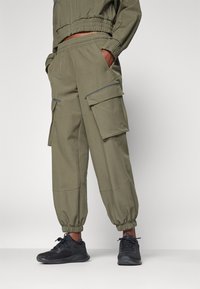 Olivgröna cargobyxor med elastiska muddar, två framfickor och sidofickor. Tillverkade av mjukt tyg med slät textur. Kombinerade med svarta sneakers.