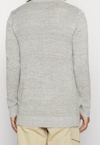 Helle graue, gerippte Strickpullover, mit langen Ärmeln und geradem Saum. Die Stofftextur ist weich und subtil variierend.