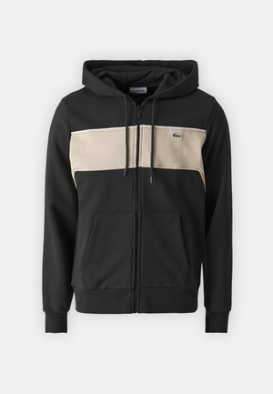 Felpa nera con zip, dotata di un pannello orizzontale crema sul petto e un piccolo logo verde. Tessuto morbido con tasche frontali.