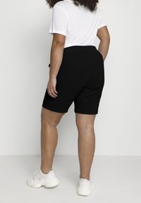 Black shorts with a relaxed fit, elastic waistband, and rolled hems, paired with a plain white t-shirt. White sneakers complete the outfit.