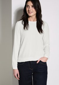 Witte, gestructureerde top met lange mouwen en een ronde hals, gecombineerd met donkere denim jeans. Eenvoudig ontwerp en relaxte pasvorm.