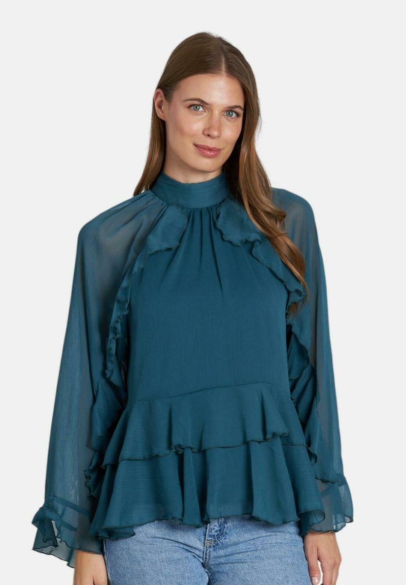 Blusa teal con dettagli a ruches, colletto alto e maniche lunghe in tessuto trasparente. Presenta strati sovrapposti e un tessuto testurizzato. Abbinata a denim.