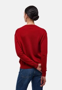 Pull en maille rouge avec un col rond, des manches longues et des poignets côtelés. Porté de face, associ é à un jean bleu. Texture douce.