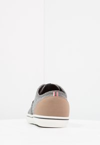 Zapatilla de tela gris con una parte trasera marrón, suela blanca y acento a rayas en el talón. Material texturizado y diseño de corte bajo.