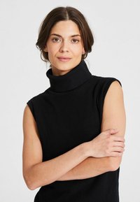 Melna bez piedurknēm turtlenecka blūze ribota dzijas audumā, ar augstu apkakli un pieguļošu siluetu. Gluda tekstūra un minimālistisks dizains.