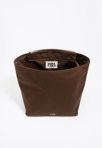 Brązowa torba na ramię z płótna o szerokim otwarciu, wyposażona w zamek błyskawiczny, wewnętrzną kieszeń oraz metkę z napisem "BIMBA Y LOLA" u góry.