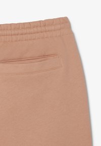 Los pantalones de chándal de color durazno presentan una textura suave, una cintura elástica y un bolsillo trasero oculto con un contorno cosido.