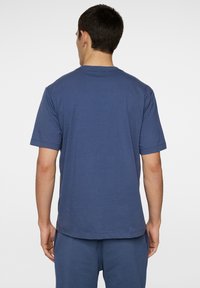 Sininen puuvillapaita lyhyillä hihoilla, pyöreällä kaula-aukkolla ja rentoa istuvuutta. Sileä pinta ja siisti helma, näkyy takaa.