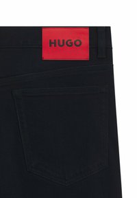Jeans in denim scuro con una toppa in pelle rossa su cui è riportato "HUGO" in lettere nere. Include una tasca posteriore con dettagli di cucitura pulita.
