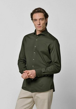 Camisa de manga larga verde oscuro con cuello estructurado, detalles de botones y un ajuste slim. La tela es suave y tiene un brillo sutil.
