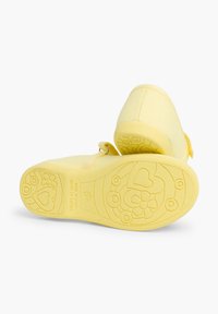 Gelbe Leinenschuhe mit Gummisohle, die mit geprägten Blumen- und Herzmustern auf der Außensohle versehen sind. Verstellbarer Riemen für einen sicheren Sitz.