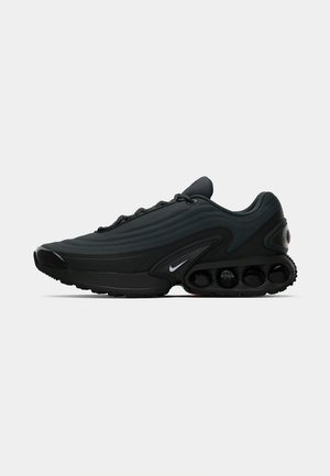 Botte de sport noire avec une tige en tissu texturé, un design courbé, une semelle intermédiaire proéminente et des éléments de rembourrage visibles. Présente un détail de logo blanc.
