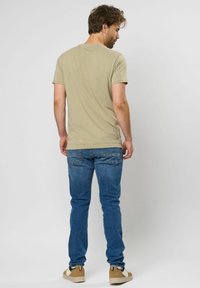 Khaki színű póló, rövid ujjú, könnyű anyagból készült. Kék farmernadrág, slim fit fazon, klasszikus öt zsebes dizájn. Hétköznapi bézs színű sportcipők, gumitalppal.