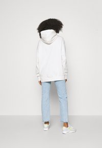 Felpa bianca con cappuccio dal fit rilassato, abbinata a jeans dritti blu chiaro e sneakers grigie con dettagli gialli.