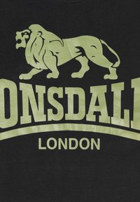 Fekete póló, nagy zöld oroszlán grafikával, alatta "Lonsdale" felirattal, a kisebb zöld betűkkel írt "London" felirattal.