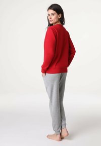 Felpa rossa con polsini a coste, abbinata a pantaloni jogger grigio chiaro con tasche laterali. Il tessuto sembra morbido e casual.