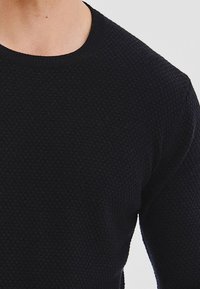 Czarny sweter z teksturowanej tkaniny z okrągłym dekoltem i długimi rękawami, wykonany z miękkiego splotu z delikatnym wzorem.