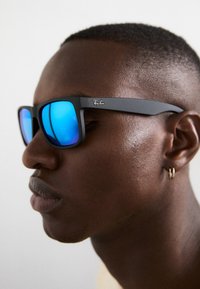 Ochelari de soare negri, cu rame pătrate și lentile blue mirror. Rame cu branding subtil și finisaj mat, cu brațe subțiri și colțuri rotunjite.