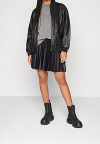 Svart läderbomberjacka över en grå topp, kombinerad med en veckad svart kjol och ankelstövlar, som har en grov sula och ögla.