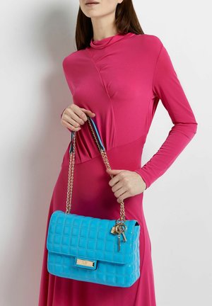 Blauwe gewatteerde handtas van glanzend materiaal, met een gouden kettinghengsel en sleutelaccenten. De tas heeft een klepafsluiting en een rechthoekige vorm.