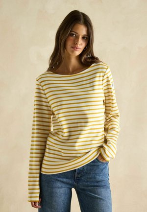Gelb-weiße gestreifte Langarmbluse mit weiter Halslinie, kombiniert mit blauen Jeans. Weicher Stoff und lockere Passform.
