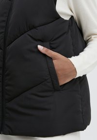 Czarna pikowana kamizelka z zamkiem błyskawicznym, z ukośnym wzorem pikowania i boczną kieszenią. Miękka w dotyku, lekka tkanina.