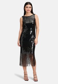 Czarna sukienka z cekinami o dopasowanej sylwetce, z frędzlami do kolan na dole i klasycznym dekoltem w łódkę. Połączona z czarnymi sandałkami na szpilce.
