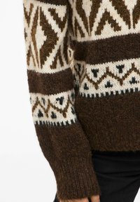 Smeđ pulover z vzorci geometrijskih oblik v krem in temno rjavi barvi, z teksturiranim pletenjem in rebrastimi manšetami.