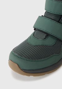Green synthetic sneaker with textured upper and rubber sole. Features velcro straps and subtle horizontal ridges on the material.