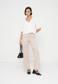 Weiße, strukturierte Bluse mit kurzen Ärmeln und V-Ausschnitt, kombiniert mit hoch taillierten, gestreiften, weit geschnittenen Hosen in Beige und Creme. Schwarze Handtasche und Schuhe.