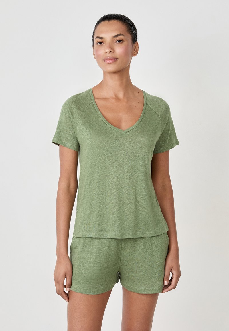 Woman wearing light green short-sleeve V-neck top and matching shorts, standing against a plain light background.