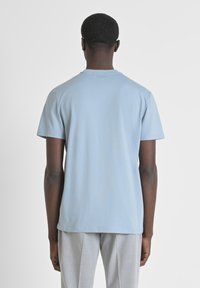 Camiseta de manga corta azul claro hecha de algodón, con un cuello redondo clásico y un corte relajado. Textura suave sin patrones ni gráficos visibles.