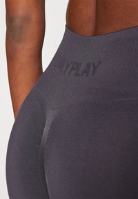 Høytlivs, mørke grå leggings med ribbestruktur og en subtil preget logo. Figurformet design fremhever form og bevegelse.