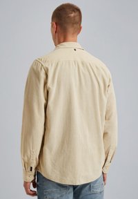 Helles beige Cordhemd mit Button-Down-Kragen und langen Ärmeln. Auffällige gerippte Textur und Knopf-Details an den Ärmeln.