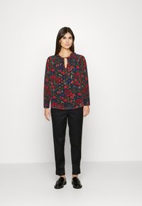 Blusa floral com rosas vermelhas sobre um fundo azul-marinho, decote em gota, mangas longas, combinada com calças pretas ajustadas e mocassins.
