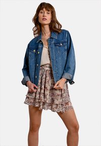 Giacca di denim di colore blu, con maniche lunghe, due tasche sul petto e chiusura a bottoni, abbinata a una gonna floreale a strati nei toni beige e rossi.