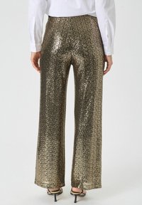 Pantalon large en sequins dorés avec une finition scintillante. Doté d'une taille haute et d'une texture lisse, complété par une fente latérale à l'ourlet.