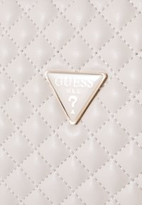Quilted grå faux læder håndtaske med en trekantet logo-plakette i guldfarve, hvor "GUESS U.S.A." er præget. Synlige syninger.