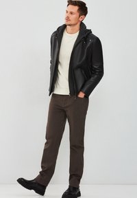 Veste en cuir noir avec capuche grise, pull crème, pantalons marron et bottes noires. La veste a des zips et des manches structurées.