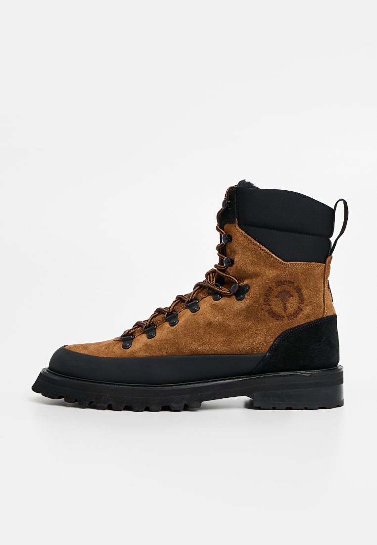 Braune Wildleder-Wanderstiefel mit schwarzen Gummielementen, Metallösen und einer strukturierten Sohle; zeichnet sich durch ein hohes Knödel-Design zur Unterstützung aus.