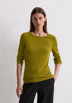 Langarm, ribbeltop in olijfgroen, met een bootneck en aansluitend ontwerp. Gecombineerd met zwarte wijde broek, tegen een neutrale achtergrond.
