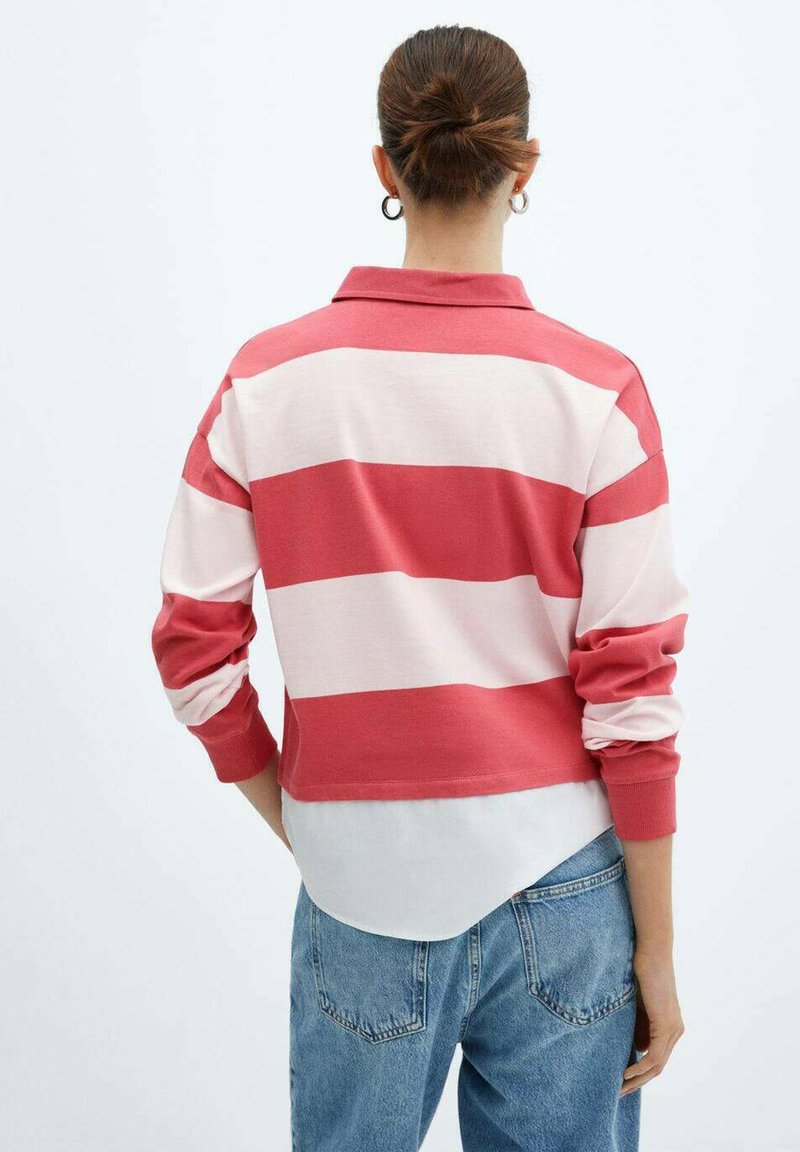 Polo a maniche lunghe a righe rosse e bianche con colletto, caratterizzato da un design cropped e polsini a coste, indossato sopra una camicia bianca e jeans blu.