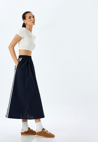 La skirti mörkblå med vita sidostripes, matchad med en åtsittande vit crop top och bruna sneakers, med vita strumpor. Slät textur.