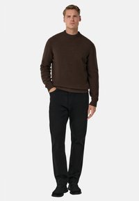 Hnědý pletený svetr s kulatým výstřihem, žebrovanými rukávy a lemem, kombinovaný s černými kalhotami s rovnými nohavicemi a černými botami. Jednoduché pozadí.