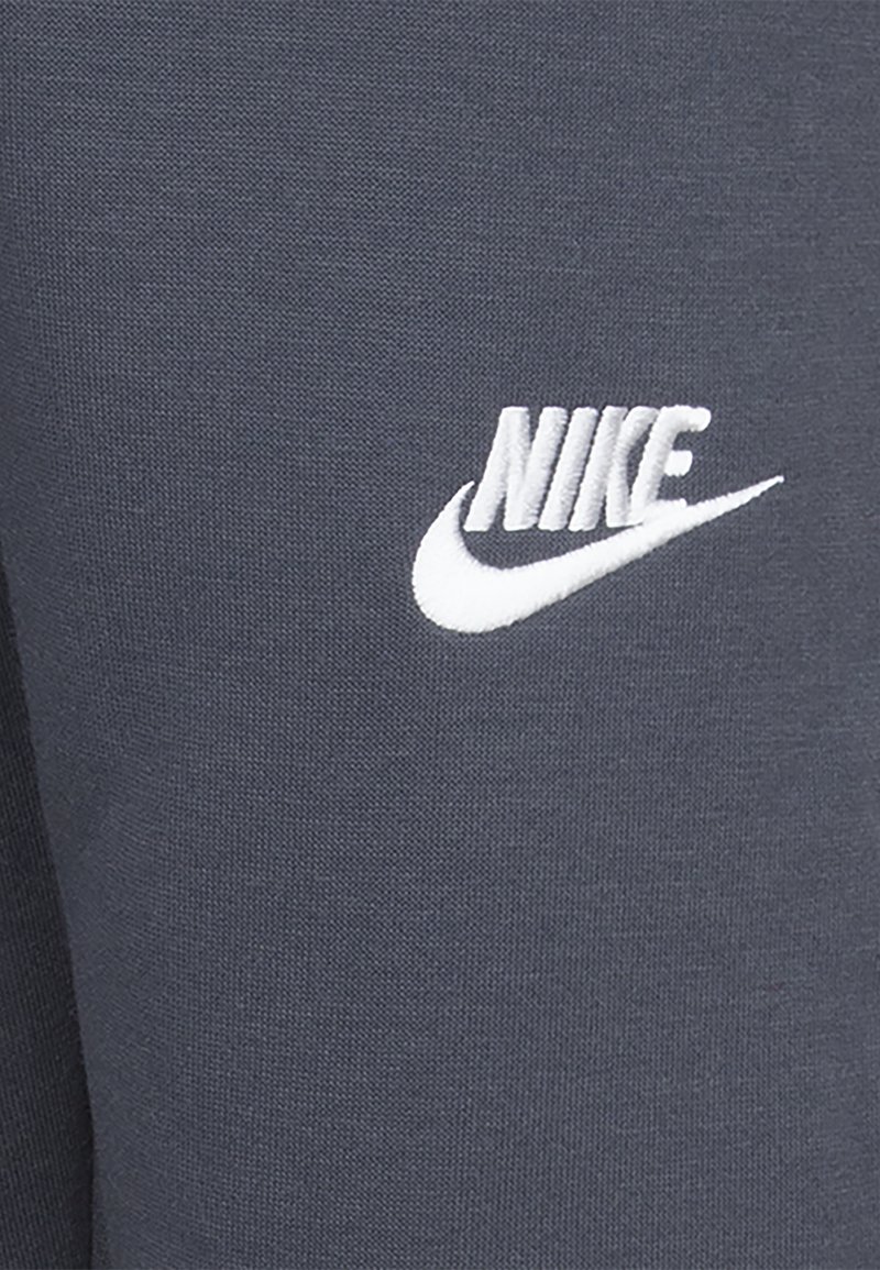 Pantalons de survêtement en coton gris avec un logo Nike brodé blanc sur la cuisse gauche. Texture lisse avec un design ajusté.
