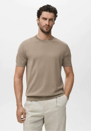 Beige short-sleeve knitted men's sweater with a round neckline and ribbed cuffs, paired with light-colored trousers.