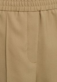 Pantalon en tissu beige avec une taille élastique, une texture subtile et une poche latérale, présenté en vue rapprochée.