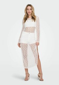 Weißes Spitzen-Zweiteiler-Outfit mit einem Langarmoberteil mit transparenten Einsätzen und einem passenden Rock, beide mit einem geometrischen Muster und einem Schlitz bis zur Mitte des Oberschenkels.