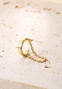Goldring mit einem glatten, runden Band, das mit einer zarten Kette verbunden ist. Der Ring hat ein offenes Design und eine glänzende, reflektierende Oberfläche.
