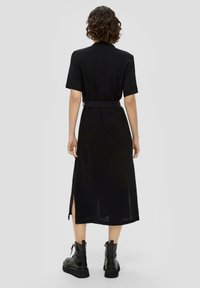 Czarna midi sukienka z krótkimi rękawami, paskiem w talii, bocznymi rozcięciami i gładką fakturą, zestawiona z masywnymi czarnymi butami wojskowymi.